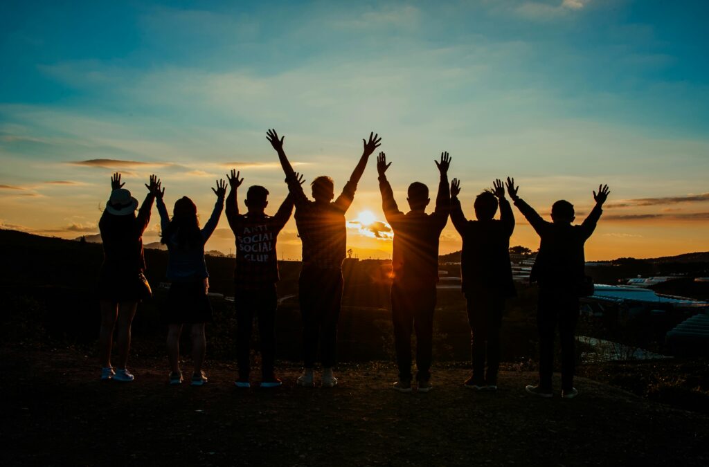 Why Group Tours Are the Smartest Way to Travel in 2025 A diverse group of friends raises their arms in celebration against a vibrant sunset backdrop.
